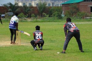 Cricket players in action on a sunny day at an outdoor field.